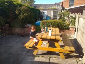 A boy sits at a yelow picnic table it is need of upcycling