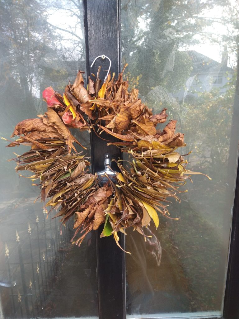 A wreath made of dried brown leaves using a coat hanger. It is hung on a black front door.