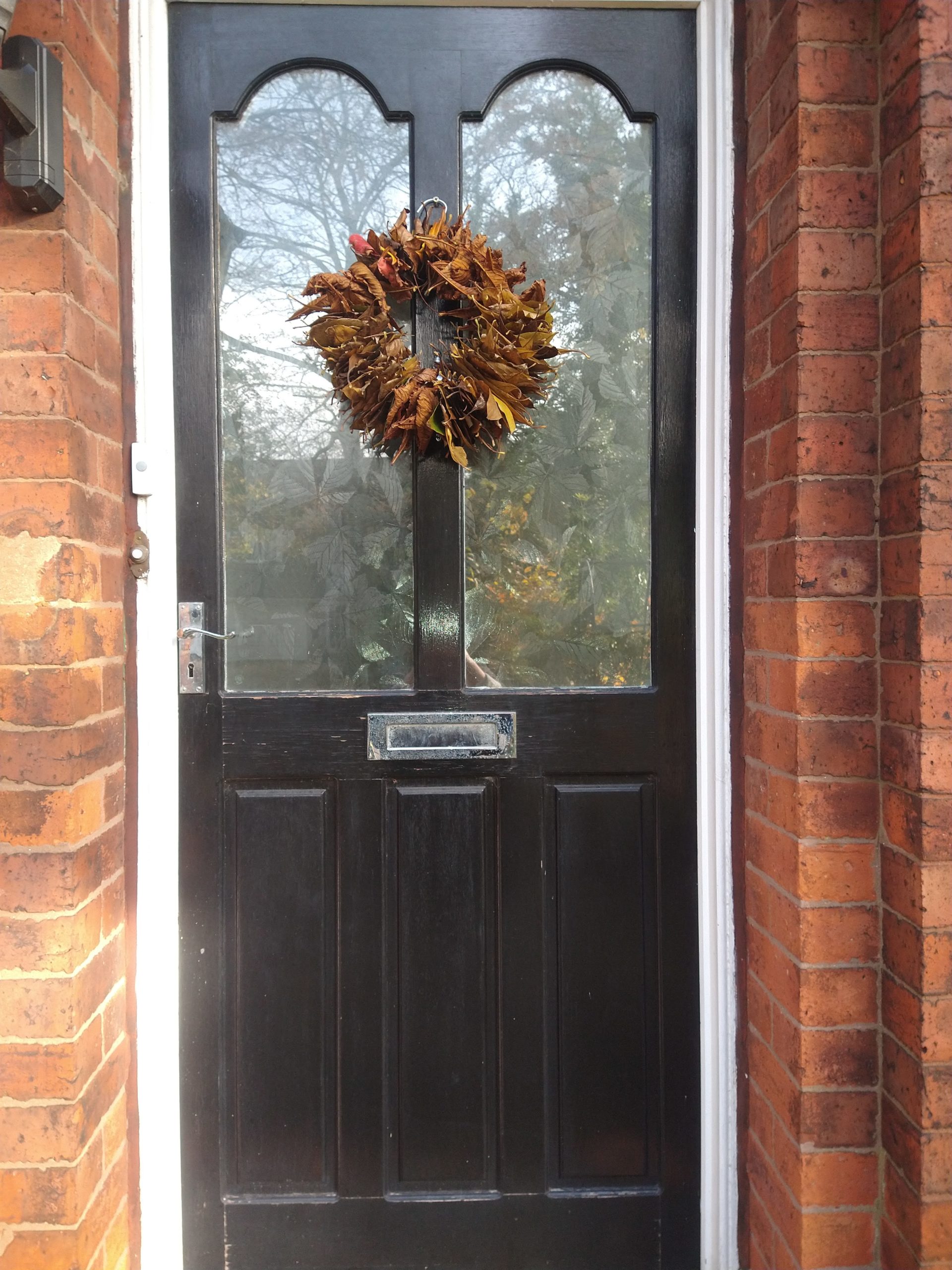 A black front door with a homemade autumnal wreath using leaves and a coat hanger.