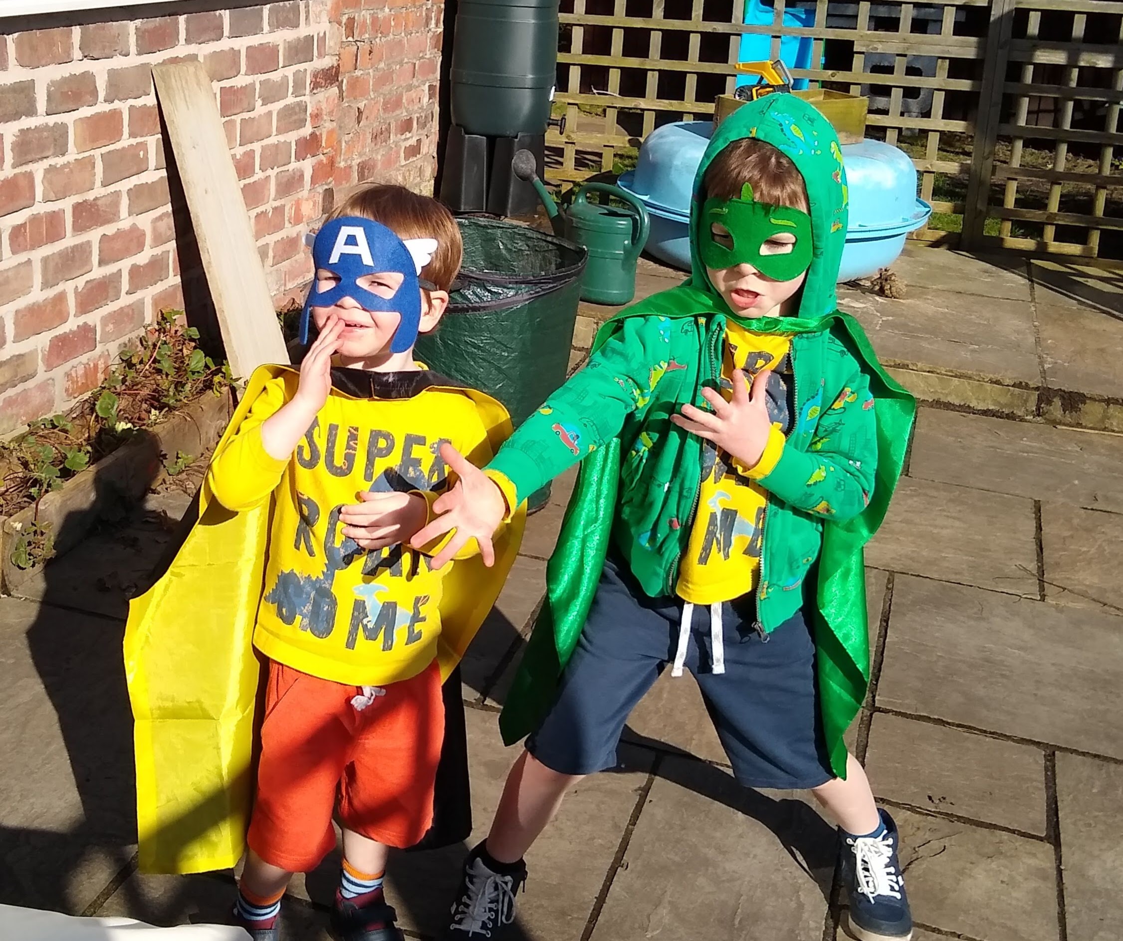 Two boys - brothers satd in super hero poses in mismatched masks and capes.