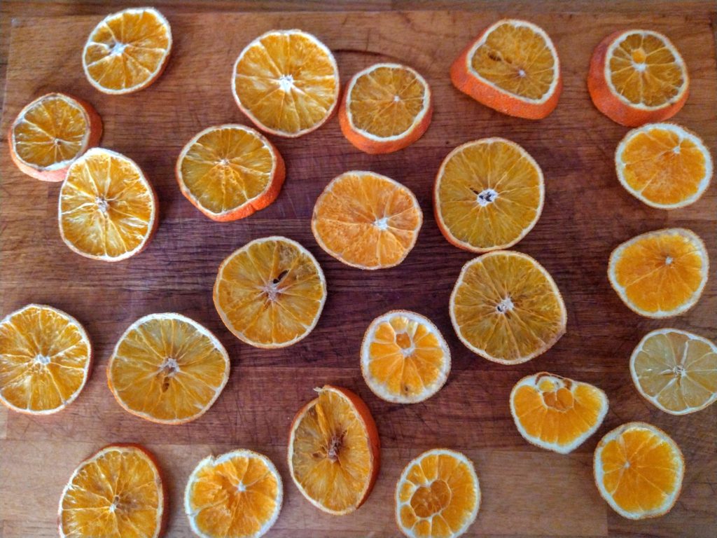 A wood surface filled with sliced oranges of all shapes and sizes. They are dried without an oven.