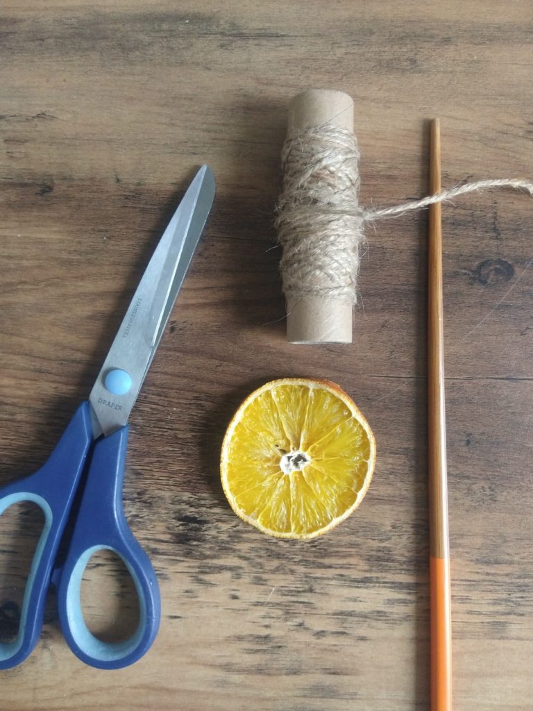 A pair of large scissors, roll of twine, an orange slice and a chop stick 