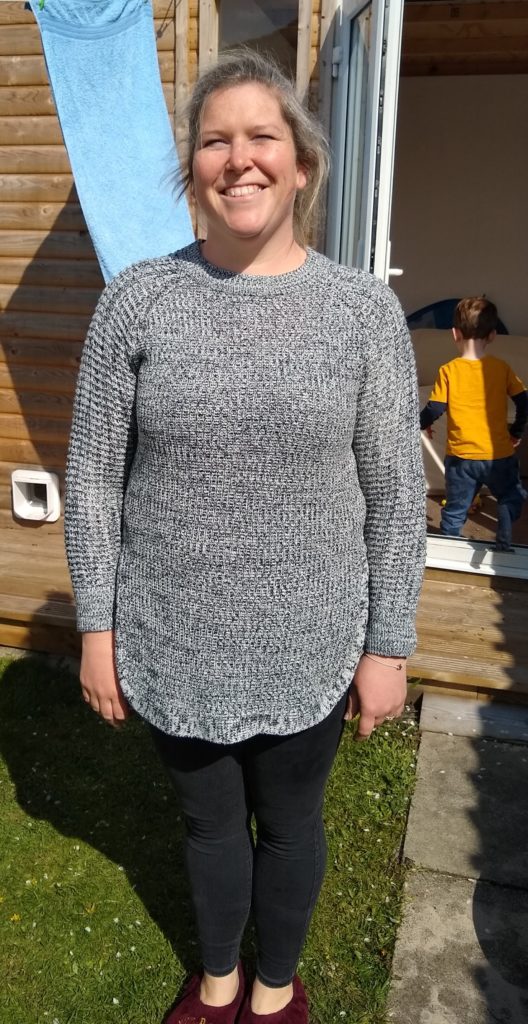 A mum stood in her garden smiling in a black and white striped jumper in tight jeans 