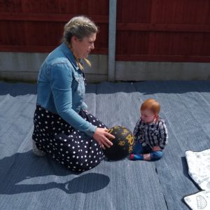 a mum sat on a mat in a garden with he 1 year old son. She i slimmer and wearing a denim jacket