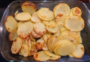 Cooked sliced peeled potatoes in a rectangular pyrex glass oven dish.