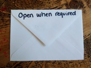 The back of a white envelope on a woden work top. Written on the envelope in black marker pen is ' open when required'
