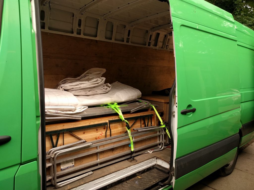 A green van with the side door open full of equipment and panel boarded.