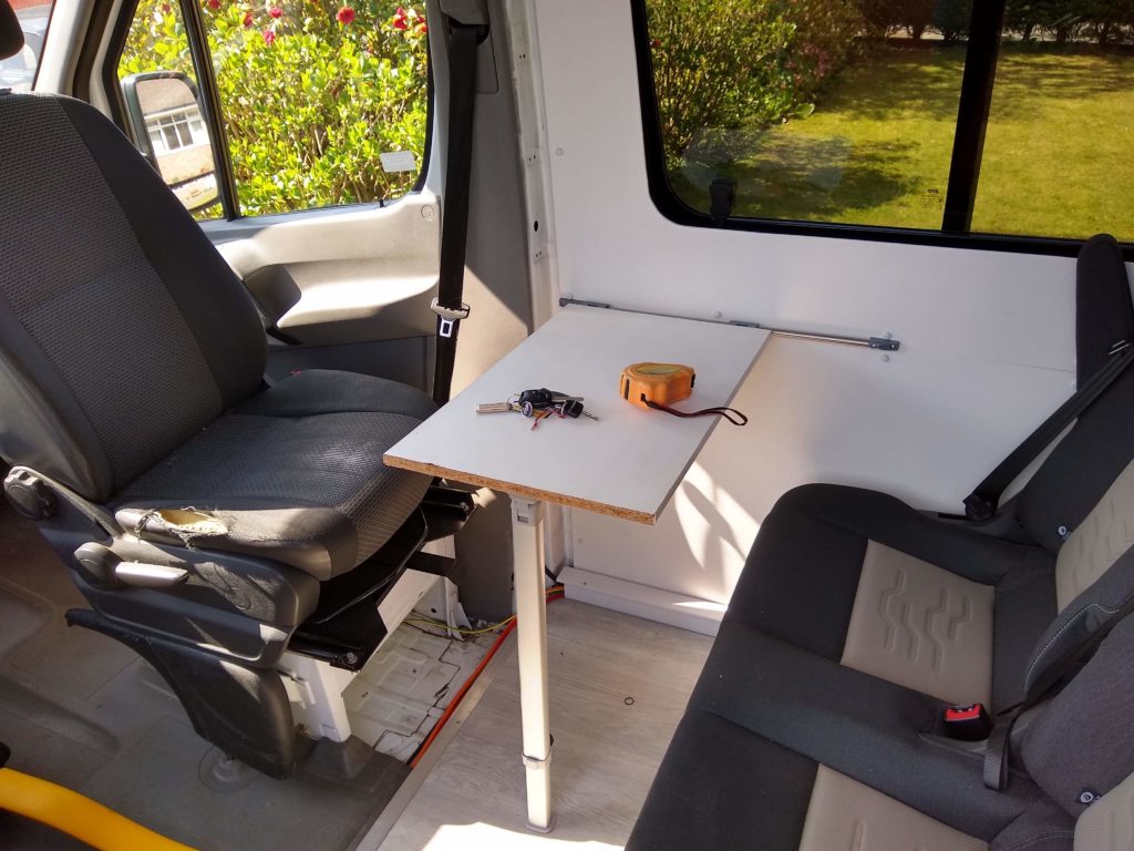 A small table inside a van. The drivers seat is swivelled round to face the two seats behind. To make a sitting /dining area.
