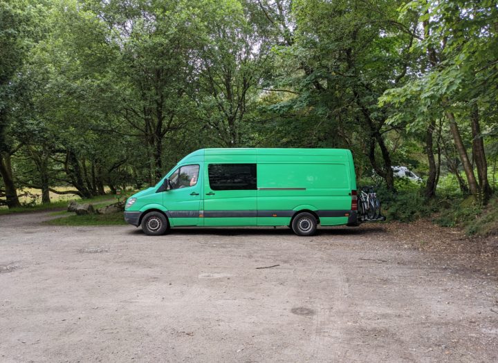A green van parked up in a car park in a forest. All alone and no one around.